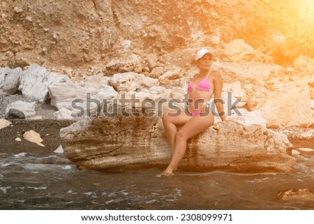 Woman travel sea. Woman traveler captures sea memory in pink bikini, posing on beach amidst volcanic mountains for adventurous journey. Happy tourist enjoys outdoor photography.