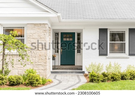 A detail of a front door on home with stone and white bricking siding, beautiful landscaping, and a colorful blue - green front door. Royalty-Free Stock Photo #2308100605