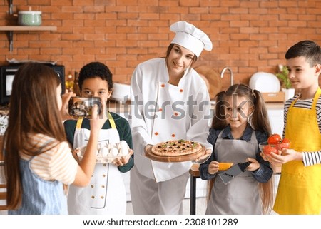 Little girl taking picture of female chef with prepared pizza after cooking class in kitchen