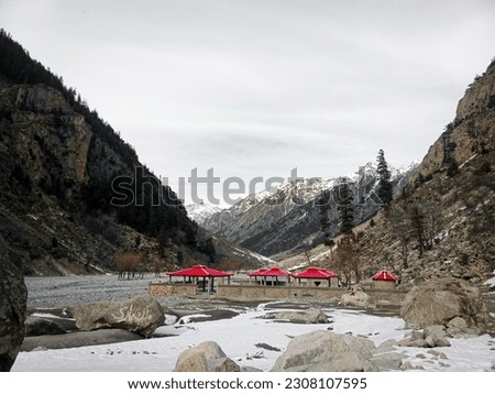 Snowcapped Mountains alongside small huts and river making peaceful scene, wallpaper.