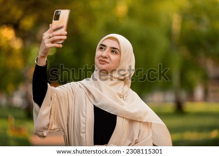 A young happy muslim woman in hijab taking selfie outside.