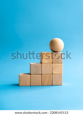 Wooden sphere on top of wood cube block bar graph chart steps on blue background, vertical style. Business growth process, trend, development, change, goal and success, economic improvement concepts.