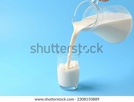 Pouring fresh milk into the glass on light blue background. Royalty-Free Stock Photo #2308150889