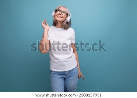 modern mature woman with gray hair listens to music in wireless headphones on studio background with copy space