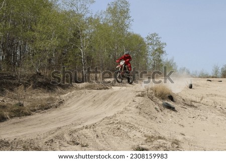 Dirt bike rider in midair on sand track jump with trees in background