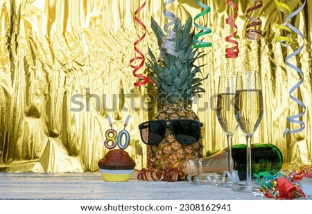 Cheerful pineapple in glasses festive happy birthday character with number  80. Beautiful background for congratulations copy space on a golden background with glasses of champagne. Anniversary 