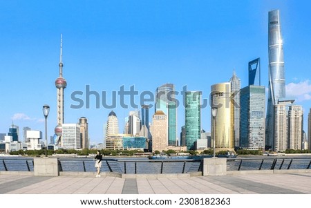 Female tourist standing against railings at Shanghai bund with the iconic Shanghai skyline view of Lujiazui behind, boat on the Huangpu River