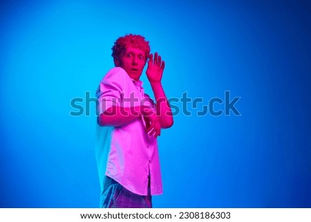 Portrait of emotive man in white shirt showing fearful face against blue studio background in pink neon light. Shock. Concept of human emotions, lifestyle, youth, facial expression