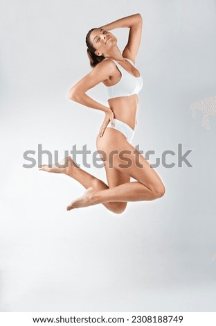 Jump, portrait and a happy woman and active in underwear isolated on a white background in a studio. Smile, carefree and a young lady in a bikini, jumping with happiness or wellness on a backdrop