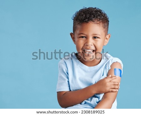 Portrait, happy and kid with plaster in studio isolated on a blue background mockup space. Face, smile and boy child with bandage after vaccine, injury or wound for healthcare, first aid and excited. Royalty-Free Stock Photo #2308189025