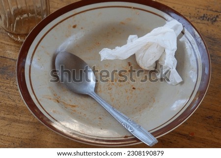 A picture of a spoon and tissue paper on a plate that has been used for eating.