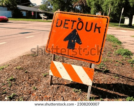 Orange detour sign on residential street with black arrow
