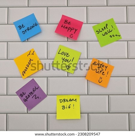 Different motivational messages written on color pieces of paper on white tile wall