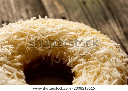 Closeup of a delicious homemade wet coconut cake with fresh coconut chips (Bolo Tapioca de Coco) on top of a rustic wooden table lit with a window in the morning, great for coffee
