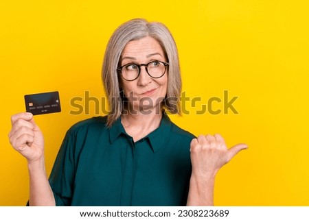 Photo of minded uncertain aged lady hold debit card look indicate finger empty space isolated on yellow color background