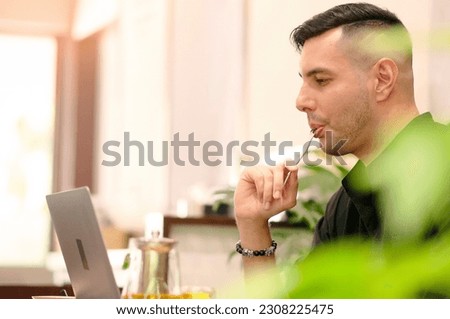 Side view of happy handsome young man eating dessert while working on laptop at home