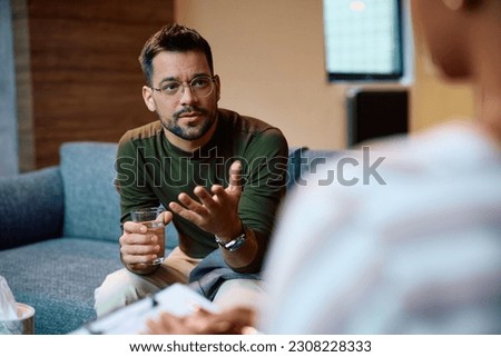 Young man talking about his issues with psychotherapist in the office. Royalty-Free Stock Photo #2308228333