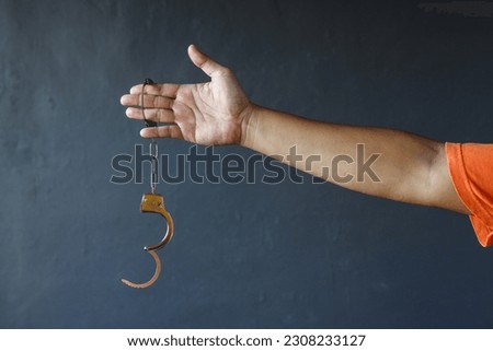 Hand of prisoner man wearing orange clothes holding opened handcuffs. Free from jail or freedom concept Royalty-Free Stock Photo #2308233127