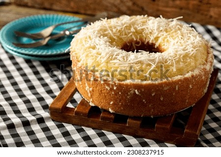 Closeup of a delicious homemade wet coconut cake with fresh coconut chips (Bolo Tapioca de Coco) on top of a rustic wooden table lit with a window in the morning, great for coffee
