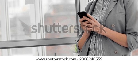 Contemporary accountant in formalwear standing by office window and messaging