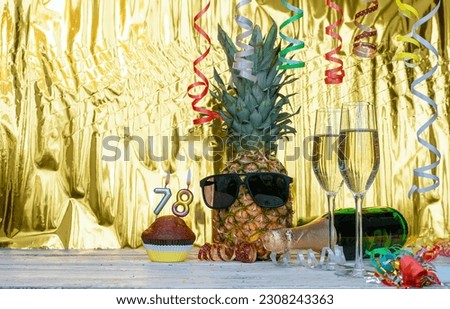 Cheerful pineapple in glasses festive happy birthday character with number  78. Beautiful background for congratulations copy space on a golden background with glasses of champagne. Anniversary