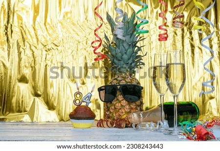 Cheerful pineapple in glasses festive happy birthday character with number  84. Beautiful background for congratulations copy space on a golden background with glasses of champagne. Anniversary