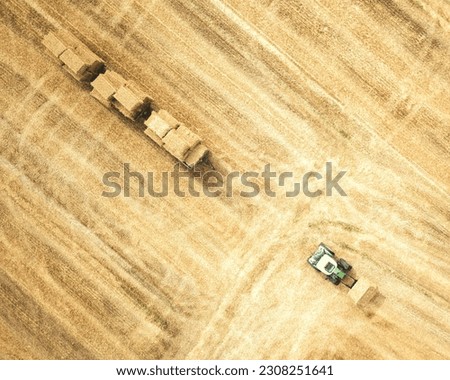 Aerial view of a green tractor loading wheat on a harvested golden farm field shot top down by a drone in germany.