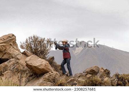 Teenage girl with a hat taking a picture of a bush, with the Teide volcano in the background, Tenerife
