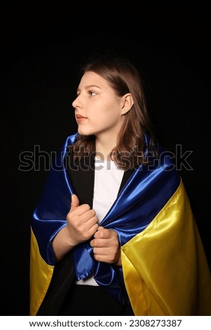 portrait of a beautiful young woman in a black blouse on a black background with the flag of Ukraine. patriot ukrainian girl with yellow and blue flag of ukraine. war in Ukraine
