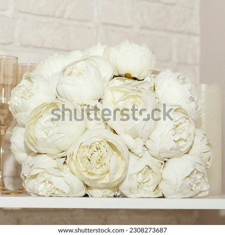 A wedding white bouquet of peonies, glasses and white candles lie on shelf. Beautiful wedding set for bride. Beautiful background,  square.