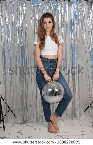 a girl in jeans and a white t-shirt and a disco ball. disco party, hen party decor. disco ball, confetti, foil curtain rain. decor for a photo shoot