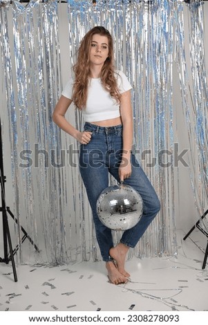 a girl in jeans and a white t-shirt and a disco ball. disco party, hen party decor. disco ball, confetti, foil curtain rain. decor for a photo shoot