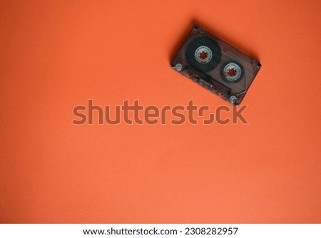 Audio cassette in the corner on orange background, top view.