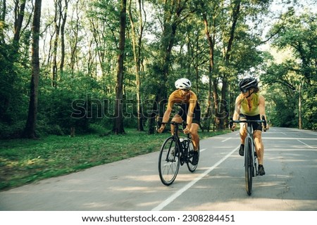 Smiling couple of riders cycling on racing bikes outside of the city. Active lifestyle and sport concept. Sporty couple of cyclist riding a bicycle on the road in the nature. Copy space. Royalty-Free Stock Photo #2308284451