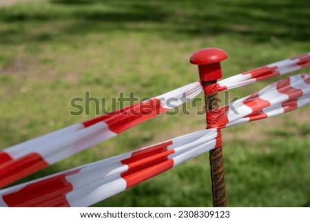 Warning tape with red and white diagonal stripes. Warn stop tape on a metal bar encloses the lawn. Red and white caution tape border. Selective focus.