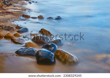 Shore with smooth water and colorful wet stones of riverbed rocks and sandy beach