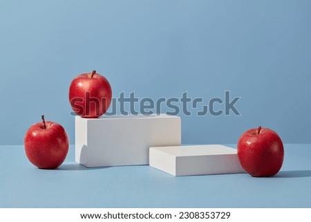 White podium in rectangle-shaped decorated with apples over a blue background. Apple (Malus domestica) helps to inhibit the increase of sebum secretion Royalty-Free Stock Photo #2308353729