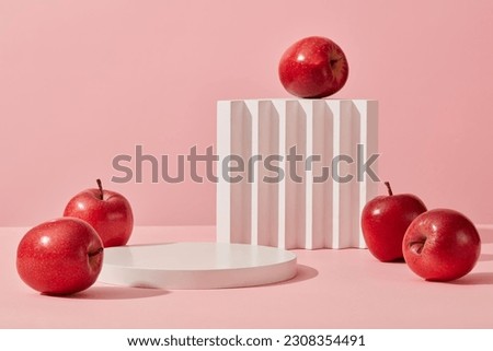 Some red apples displayed on a pink background with cylinder white podiums. Abstract background with minimalist style for product brand presentation. Advertising cosmetic from apple ingredient