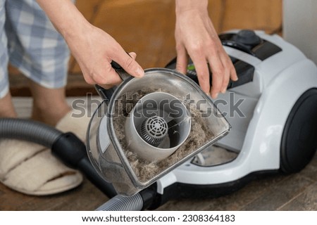  Woman holding household vacuum cleaner container clogged up with wool of domestic animals, fur, hair and dust after an extensive cleaning. Cause of allergies, asthma exacerbation, frequent cleaning. Royalty-Free Stock Photo #2308364183