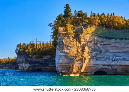 Submerged cave at pictured rocks national park with golden sunlight striking cliff face above lake