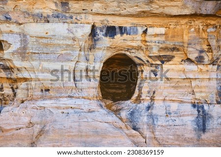 Cave opening in Pictured Rocks cliff wall of gold, rust, and mineral colors