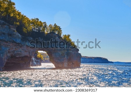 Sunny waters on great lake with archway in pictured rocks and green forest atop the cliff walls