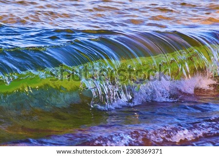 Cresting wave with green and white within the water crashing against the shore