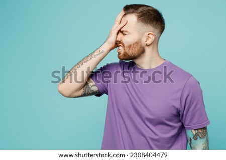 Young sad man he wearing purple t-shirt put hand on face facepalm epic fail mistaken omg gesture isolated on plain pastel light blue cyan background studio portrait. Tattoo translates life is fight