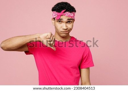 Young dissatisfied upset sad man of African American ethnicity he wear headscarf t-shirt casual clothes showing thumb down dislike gesture isolated on pastel plain light pink color background studio Royalty-Free Stock Photo #2308404513