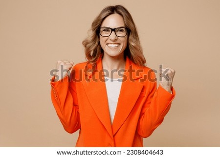 Young successful employee business woman corporate lawyer wear classic formal orange suit glasses work in office do winner gesture celebrate clenching fists isolated on plain beige background studio Royalty-Free Stock Photo #2308404643