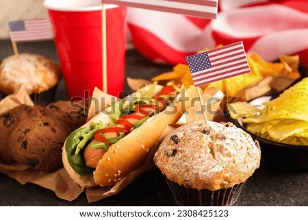 Tasty hot dog, cookies, muffins and snacks for Memorial Day celebration on dark table, closeup