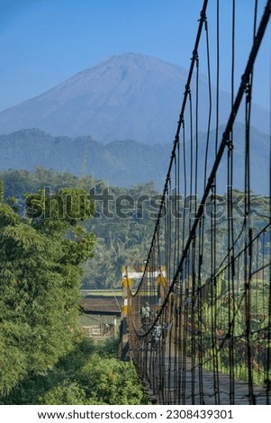 Wooden suspension bridge over the river with beautiful mountain views. Rural scene of Indonesian countryside - Magelang, Indonesia