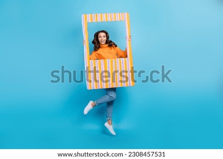 Full length photo of cute impressed woman wear orange sweater jumping high tacking photo isolated blue color background