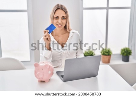 Young woman using credit card and laptop sitting on table at home